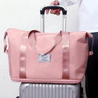 Pink duffel bag with front patch label, reinforced webbing handles, and top zip; on suitcase.