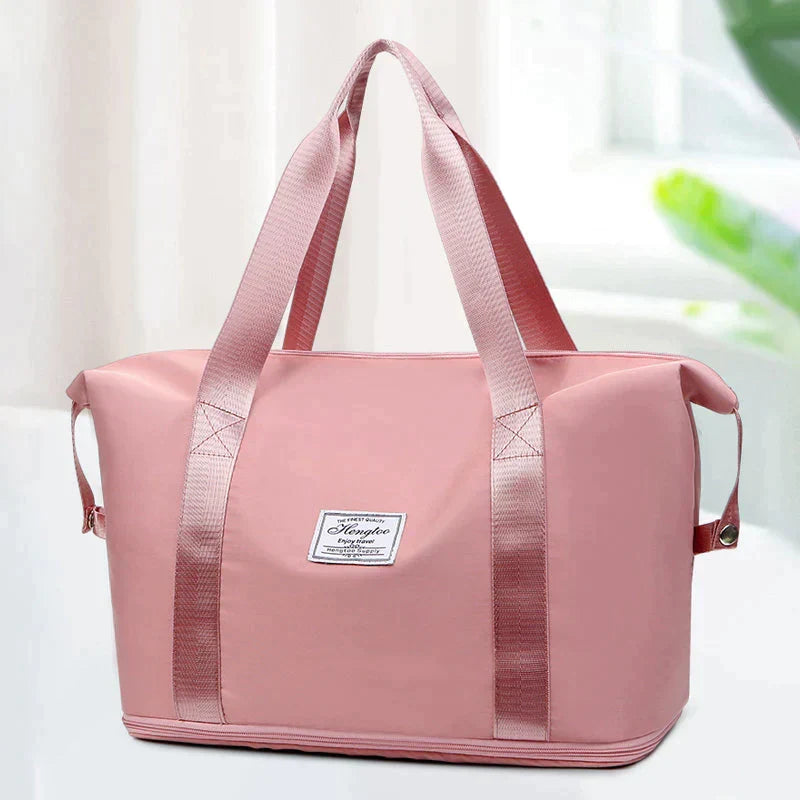 Pink duffel bag with long handles, front patch label, and striped trim along base.