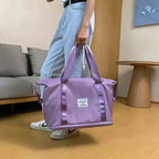 Purple duffel bag held by a person, wide base, front patch label, and top zip closure.