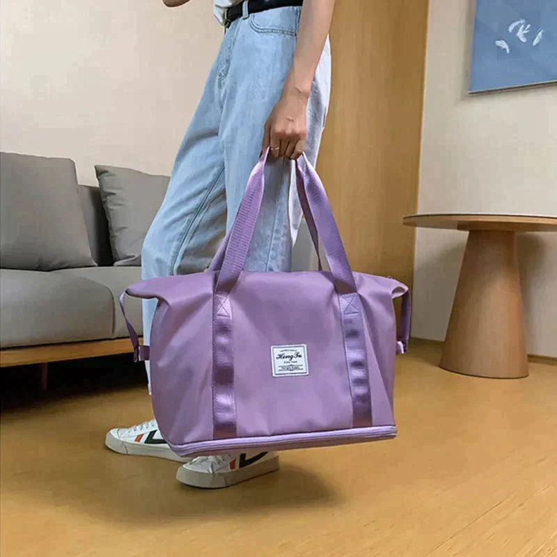 Purple duffel bag held by a person, wide base, front patch label, and top zip closure.