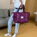 Purple duffel bag carried by a person with long handles, wide base, and front patch label.